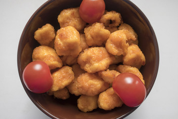 Appetizing and delicious fried chicken pieces in batter served in a deep plate on a light background close-up and cherry tomatoes