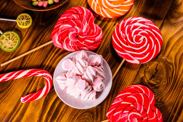 Ceramic plate with marshmallow, candy cane and lollipops on a wooden table. Top view
