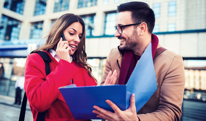 Business people in front of the corporation. Businesswoman talking on a mobile phone while her colege watching documents in folder. Business, education, lifestyle concept