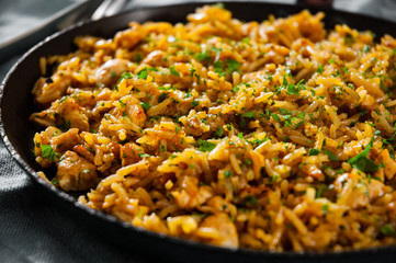 Chicken Breast with Rice and vegetables in a frying pan on dark wooden background