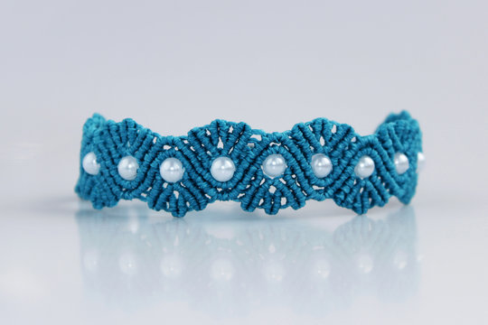 turquoise bracelete with white beads for the hand from waxed thread in the technique of macrame on a white background