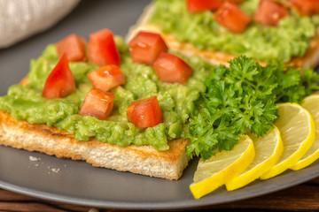 Fototapeta na wymiar close up of sandwiches with latin american mexican sauce guacamole avocado and white bread toast decorated chopped tomatoes, sliced lemon on plate, vegetarian food
