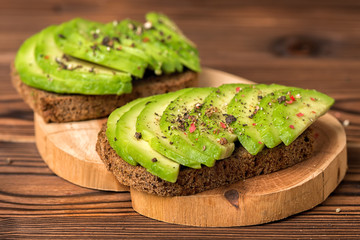 avocado sandwiches with rye bread toast and peppered on wooden background, healthy organic food concept