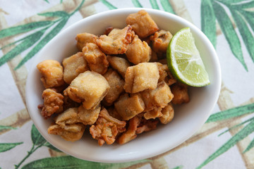 White dish of fried fish and lemon on table with white and green towel.