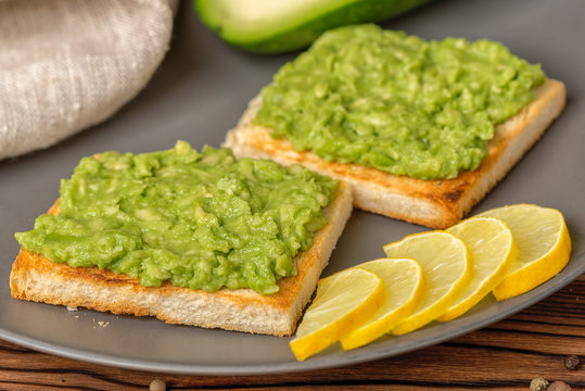 sandwiches with latin american mexican sauce guacamole avocado and white bread toast decorated sliced lemon on wooden background, vegetarian food