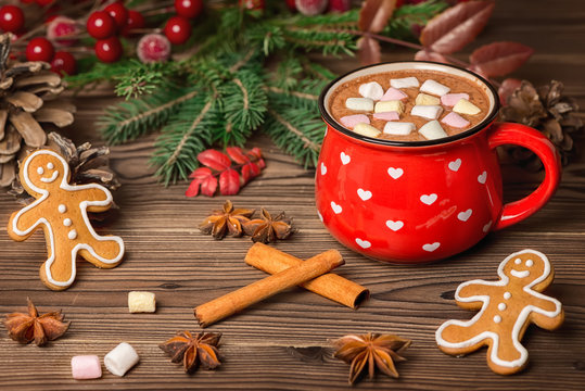 hot cocoa with marshmallow candies, gingerbread cookies decorated Christmas tree branch, cones, cinnamon and anis on wooden, festive background