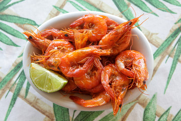 White dish of fried shrimp with paprika and lemon on table with white and green towel.