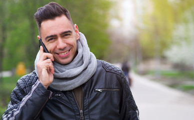 Young happy man talking on a smart phone standing in a park.