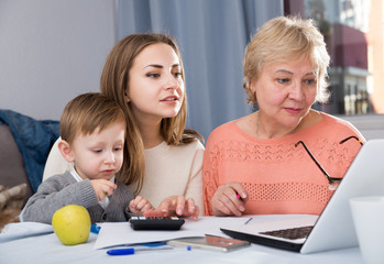 Aged woman is mastering technology near laptop with her daughter and grandson