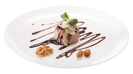Chocolate ice cream ball decorated with chocolate syrup, mint leaves and almond slices on a white plate