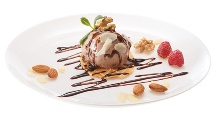 Chocolate ice cream ball decorated with chocolate syrup, raspberries, mint leaves and almond slices on a white plate