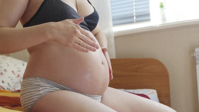 Anonymous pregnant woman stroking her stomach. Body and skin care.