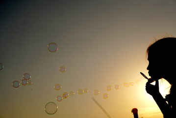 Silhouette of the girl blowing bubbles against the background of the sunset