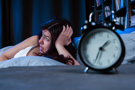 Photo of unhappy woman with insomnia lying on bed next to alarm clock