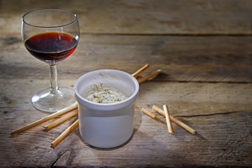potted blue stilton cheese in a ceramic jar, port wine and some nibble sticks on a dark rustic...