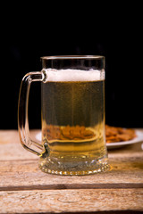 On the wooden table is a mug with a light beer. In the background is a plate with crispy croutons. Close-up.