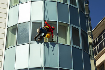 rope access technician in a helmet washes the window of a high-rise building from the outside, hanging on a rope