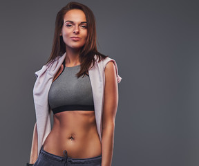 Obraz premium Slim fitness brunette woman in a gray sportswear posing in a studio.