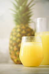 Pineapple juice in glassware and whole pineapple fruit on gray background. Copy space, sunlight effect. Summer, holiday concept. Raw, vegan, vegetarian, clean eating diet.