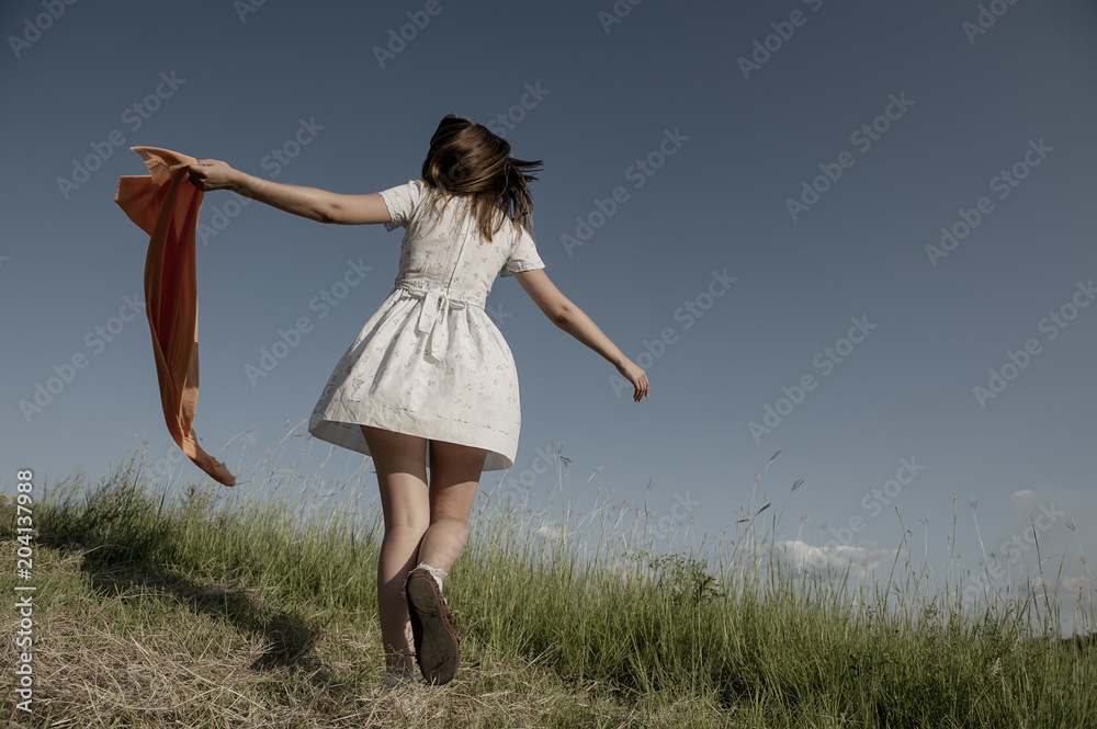 Wall mural BEAUTIFUL BLONDE GIRL LAUGHS AND DANCES OUTDOORS WITH AN ORANGE SCARF IN HER HANDS