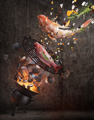 Kettle grill with hot briquettes, cast iron grate and tasty sea fishes flying in the air.