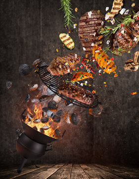 Kettle grill with hot briquettes, cast iron grate and tasty beef steaks flying in the air.