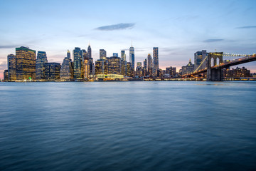 Night view of Manhattan skyline and Brooklyn Bridge on top of the Hudson river. New York City, USA.
