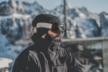 Portrait of bearded handsome snowboarded in sunglass mask, at the ski resort on the background of mountains and blue sky.Blurred background.Horizontal.Color mask