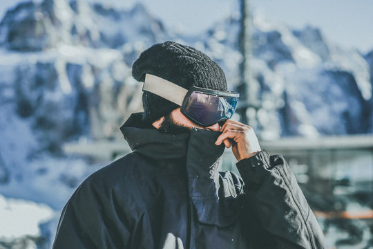 Portrait of bearded young snowboarded in sunglass mask, at the ski resort on the background of mountains and blue sky.Blurred background.Horizontal image.