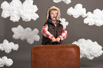 boy dressed as an airplane pilot stand between the clouds with old suitcase and playing with handmade plane