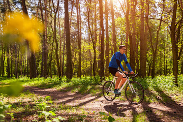 Obraz premium Young man bicyclist riding a road bike in spring forest