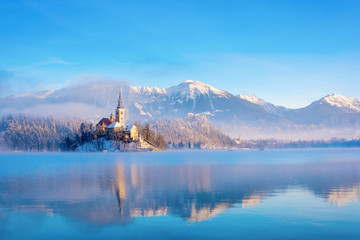 Lake bled on a winter sunny morning with clear sky and snow covering the mountains - obrazy, fototapety, plakaty