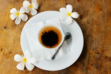 White cup of ceylon tea and yellow exotic flowers Plumeria - flat lay Sri Lanka's background with wooden old table.