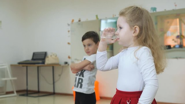 Children's developing a game room. Emotions of young children during entertaining classes. blonde curly child is drinking water from a transparent glass.