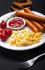 Wiener Sausages and scrambled eggs in a dish on black background.