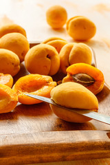 The process of manual cleaning of apricots from bones using a kitchen knife on a wooden dish. Preparation for cooking jam. Lifestyle