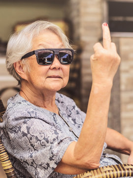 Cool old lady, wearing sunglasses, expressing herself showing the middle finger.