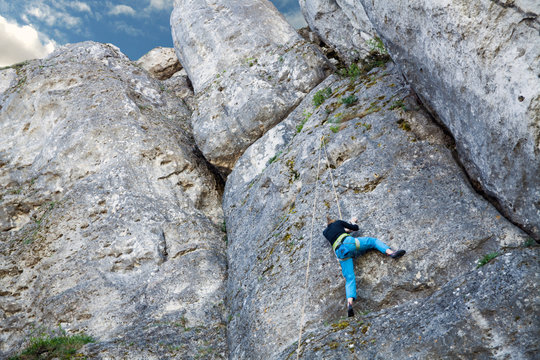 The woman climbs to the top of the mountain. A young girl on a climbing wall under the open sky. Climbing the rope and climb the mountain.The woman climbs to the top of the mountain. 