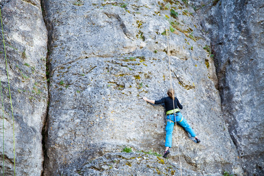 The woman climbs to the top of the mountain. A young girl on a climbing wall under the open sky. Climbing the rope and climb the mountain.