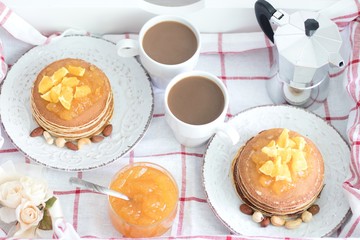 Obraz na płótnie Canvas Breakfast for two. American pancakes with orange jam and nuts on vintage plates and 2 white coffee cups. Top view