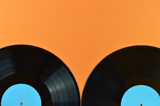 parts of two old black vinyl records with blank cyan labels on orange background
