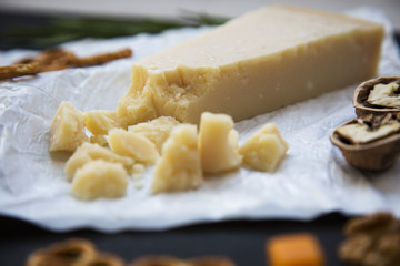 Tasting parmesan cheese with walnuts and pretzels on dark background. Food for wine. Closeup.