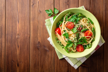 Spaghetti pasta with green beans, peas, cherry tomatoes, parsley and parmesan cheese on wooden table