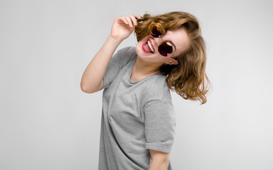 Charming young girl in a gray T-shirt on a gray background. Cheerful girl in round glasses