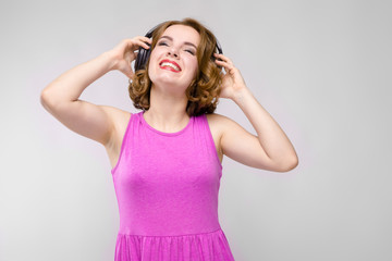 Charming young girl in pink dress on gray background. Young girl with headphones smiling