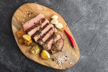 Grilled beef steak with spices, garlic, rosemary and chili pepper on cutting board. Top view.  Copy space. Stone background