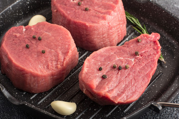 Raw beef meat with rosemary and garlic on a grill pan. Close-up
