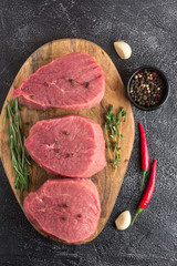 Raw beef meat with rosemary, thyme and chili pepper on a cutting board. Stone background. Top flat view. Vertical view