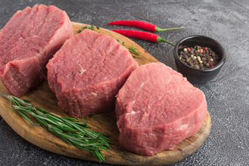 Raw beef meat on a cutting board with rosemary, spices and chili pepper. Gray stone background. Close up