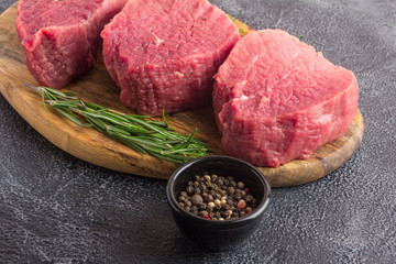 Raw beef meat on a cutting board with rosemary and spices. Gray stone background